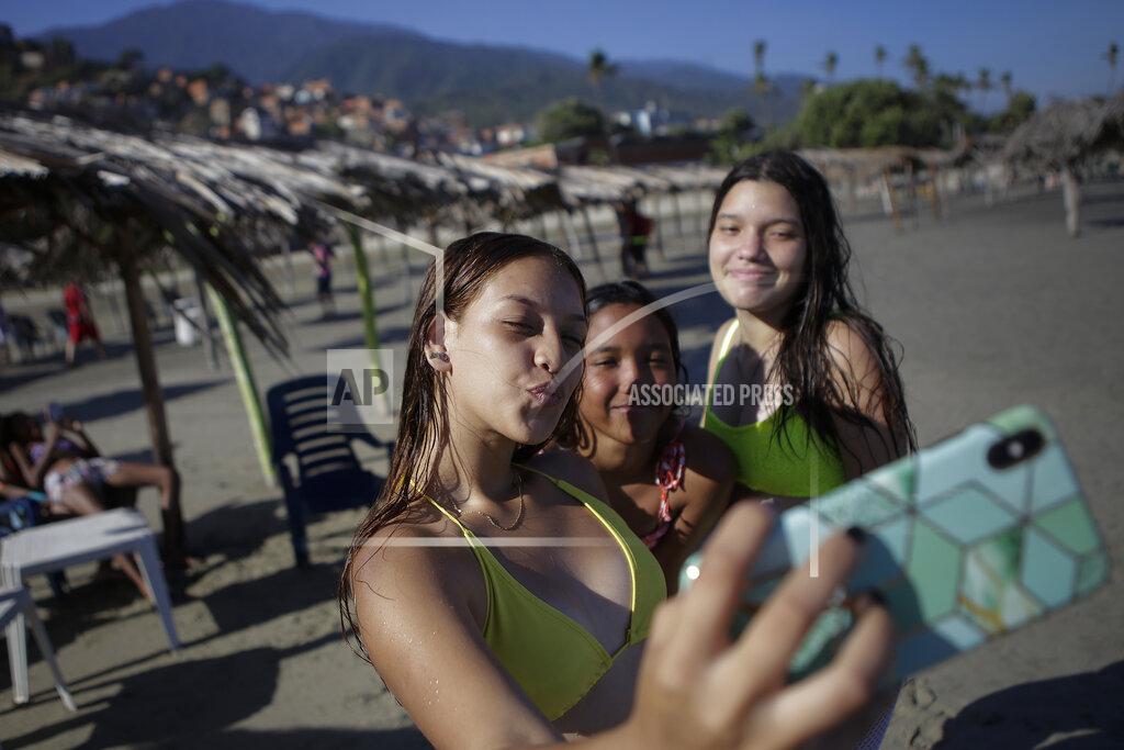 Matias Delacroix Friends take photos of themselves on La Ultima beach which was reopened this week after it was closed for months amid the COVID-19 pandemic in La Guaira, Venezuela, Friday, Oct. 23, 2020. Strict quarantine restrictions forced the closure of beaches across the country in March and reopened this week in hopes of revitalizing the battered economy. (AP Photo/Matias Delacroix)