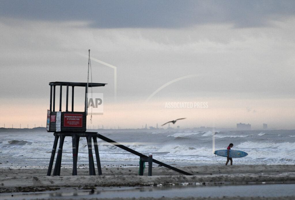 A surfer walks on the beach at J.P. Luby Park ahead of Tropical Storm Hanna, Friday, July 24, 2020, in Corpus Christi, Texas. The storm is expected to make landfall on Saturday. (Annie Rice/Corpus Christi Caller-Times via AP)