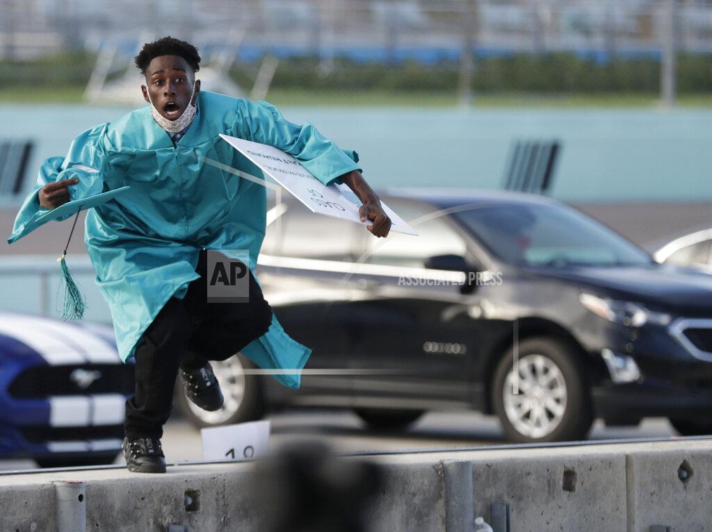 Wilfredo Lee FILE - In this June 23, 2020, file photo, Richardson Fremond leaps over a wall as he runs to collect an award during a graduation ceremony for the senior class of Chambers High School at Homestead-Miami Speedway, in Homestead, Fla. Forty-one seniors graduated from the school and crossed the start-finish line to receive their diplomas, during the coronavirus pandemic. (AP Photo/Wilfredo Lee, File)