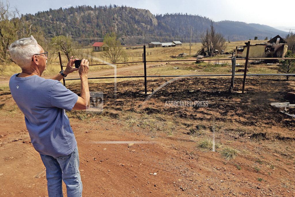 Luis Sanchez Saturno A.B. Montoya takes a photo of a building that was completely burned in the Calf Canyon Fire in Rociada, N.M., Tuesday, May 10, 2022. The former owner of this house was related to his dad. The largest wildfire burning in the United States was heading toward mountain resort towns in northern New Mexico on Wednesday, prompting officials to issue another set of warnings for more people to prepare to evacuate as the fast-moving fire picks up momentum. (Luis Sanchez Saturno/The New Mexican via AP)