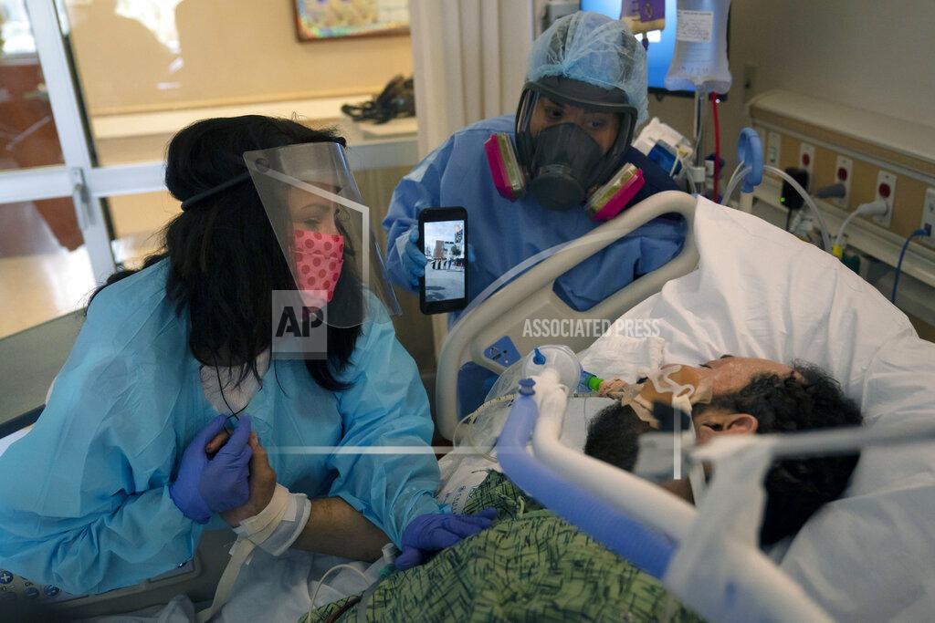 Jae C. Hong FILE - In this Feb. 15, 2021, file photo, Patty Trejo, 54, left, looks at her intubated husband, Joseph, in a COVID-19 unit as registered nurse Celina Mande holds a smartphone showing a mariachi band performing for the patient at St. Jude Medical Center, in Fullerton, Calif. Trejo visited her husband for the first time since he was hospitalized more than a month ago. A survivor of COVID-19 herself, she invited a mariachi band to give him courage. Surrounded by hospital staff, family members and friends in the parking lot of the hospital, the band played her husband's favorite song, "La mano de Dios," or "The Hand of God." "He needs to know that I still love him, and he needs to know he's got to fight," said Trejo. (AP Photo/Jae C. Hong, File)