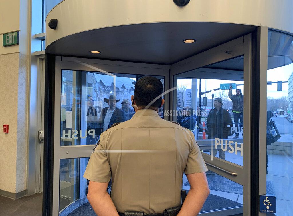 Rebecca Boone Anti-government activist Ammon Bundy, wearing a cowboy hat, yells through the closed Ada County Courthouse door at law enforcement officers inside Monday, March 15, 2021, in Boise, Idaho. Bundy was scheduled to stand trial Monday on charges that he trespassed and obstructed officers at the Idaho Statehouse during a special legislative session last fall, but Magistrate Judge David Manweiler issued a warrant for Bundy's arrest after Bundy failed to appear in the courtroom. People are required to wear face coverings while at the courthouse because of the coronavirus pandemic, but Bundy and several others were protesting the mask requirement. (AP Photo/Rebecca Boone)