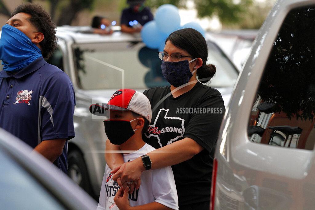 Cedar Attanasio In this Thursday, May 21, 2020 photo, Vanessa Romero holds her son at a memorial service for the 23rd victim of the Aug. 3 Walmart shooting while wearing an "El Paso Strong" T-shirt and a face mask in El Paso, Texas. Guillermo "Memo" Garcia died from bullet wounds after nine months in the hospital. The "El Paso Strong" slogan united residents after the shooting, but hasn't caught on in the fight against COVID-19. (AP Photo/Cedar Attanasio)