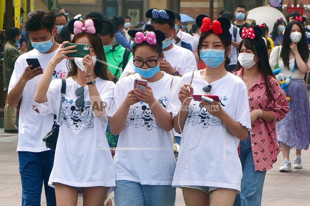 Visitors, wearing face masks, enter the Disneyland theme park in Shanghai as it reopened, Monday, May 11, 2020. Visits will be limited initially and must be booked in advance, and the company said it will increase cleaning and require social distancing in lines for the various attractions.(AP Photo/Sam McNeil)