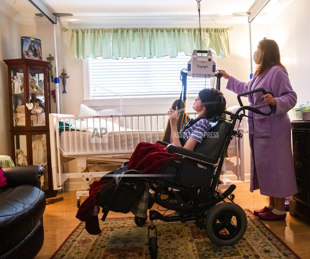 Sophia Germer Lisa Haynes, a direct support worker, helps get Lauren, who has cerebral palsy and is non-verbal, into her bed at the home of Sue Roesky in Metairie, La., Friday, Sept. 17, 2021. Haynes is one of four people to help Roesky care for Lauren. (Sophia Germer/The Times-Picayune/The New Orleans Advocate via AP)