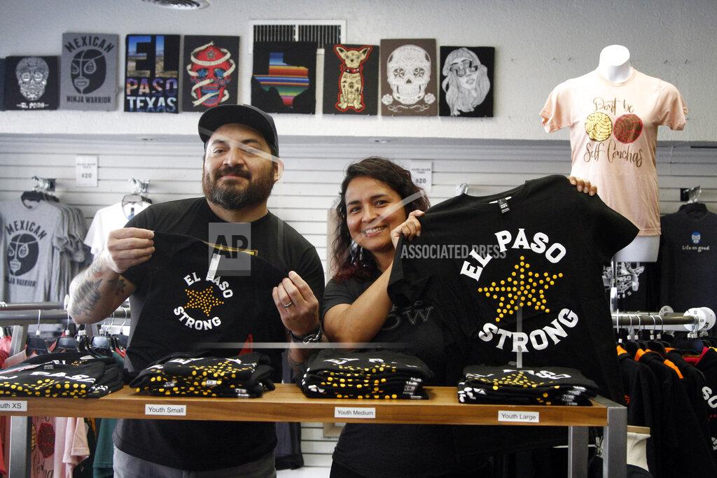 Cedar Attanasio In this Thursday, May 21, 2020 photo, artists Charlie Monarrez, 46, and Monica Monarrez, 36, hold up "El Paso Strong" clothing at the print shop where they work in El Paso, Texas. Charlie designed the print after the Aug. 3 mass shooting using a slogan that united the city. Monica said she worked so hard printing the shirts and selling them to raise money for the shooting's dozens of victims that she was hospitalized with exhaustion after two weeks. (AP Photo/Cedar Attanasio)