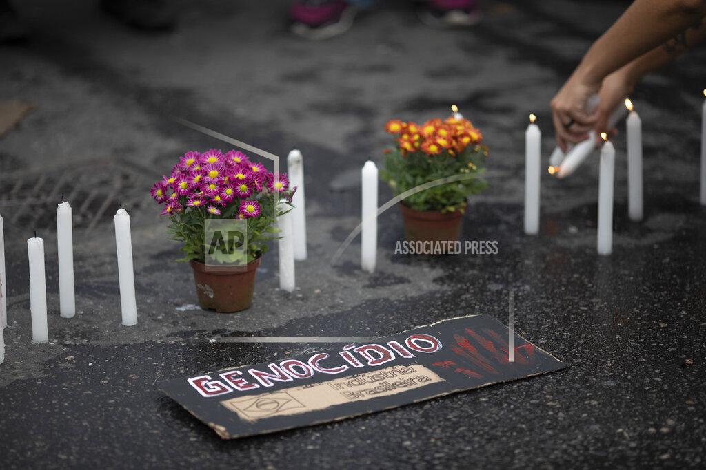 Silvia Izquierdo A woman light candles near a sign that reads "Genocide" the day after a deadly police operation in the Jacarezinho favela of Rio de Janeiro, Brazil, Friday, May 7, 2021. A bloody, hourslong gunbattle here echoed into Friday, with authorities saying the police mission killed two dozen criminals while residents and activists claimed human rights abuses. (AP Photo/Silvia Izquierdo)