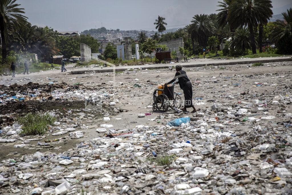 Rodrigo Abd A woman pushes a wheelchair, carrying her empty water containers, through an empty street littered with trash near the judiciary and legislative buildings, in Port-au-Prince, Haiti, Tuesday, Sept. 22, 2021. Most of the population of Port-au-Prince has no access to basic public services, no drinking water, electricity or garbage collection. (AP Photo/Rodrigo Abd)