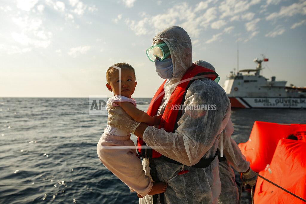 Emrah Gurel A Turkish coast guard officer, wearing protective gear to help prevent the spread of coronavirus, carries a child off a life raft during a rescue operation in the Aegean Sea, between Turkey and Greece, Saturday, Sept. 12, 2020. Turkey is accusing Greece of large-scale pushbacks at sea — summary deportations without access to asylum procedures, in violation of international law. The Turkish coast guard says it rescued over 300 migrants "pushed back by Greek elements to Turkish waters" this month alone. Greece denies the allegations and accuses Ankara of weaponizing migrants. (AP Photo/Emrah Gurel)