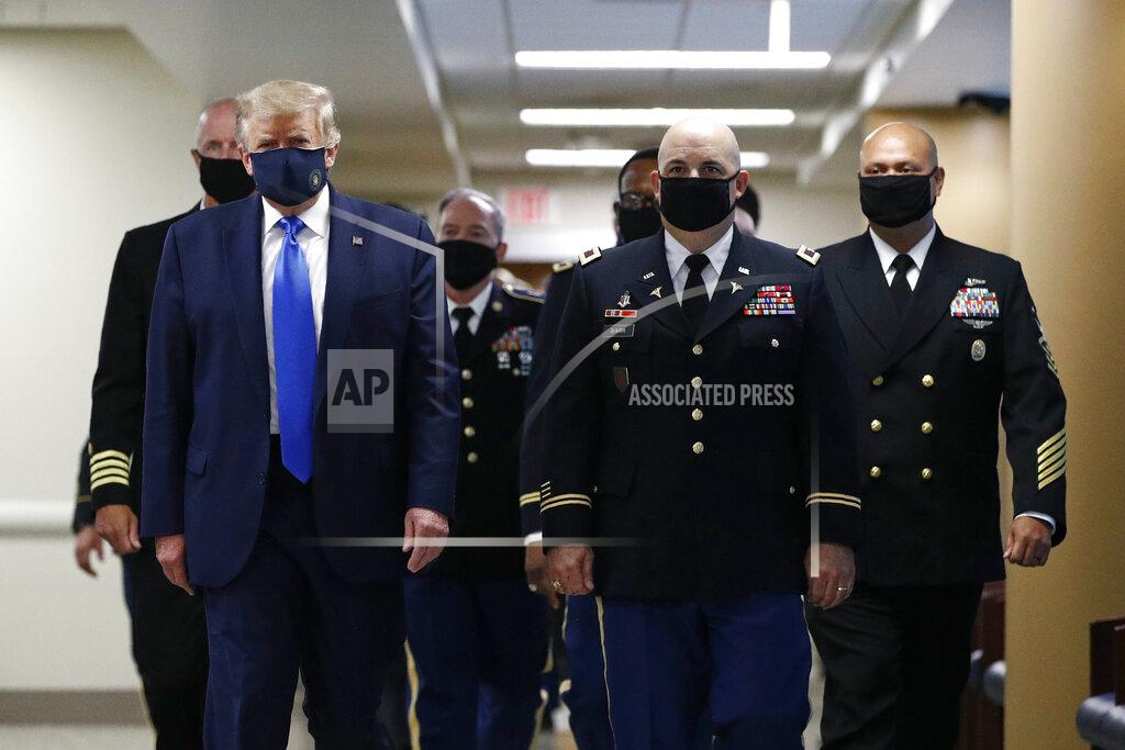 FILE - In this July 11, 2020, file photo President Donald Trump, foreground left, wears a face mask as he walks with others down a hallway during a visit to Walter Reed National Military Medical Center in Bethesda, Md. On Tuesday, July 21, Trump professed a newfound respect for the protective face masks he has seldom worn. “Whether you like the mask or not, they have an impact," he said. "I’m getting used to the mask,” he added, pulling one out after months of suggesting that mask-wearing was a political statement against him. (AP Photo/Patrick Semansky, File)
