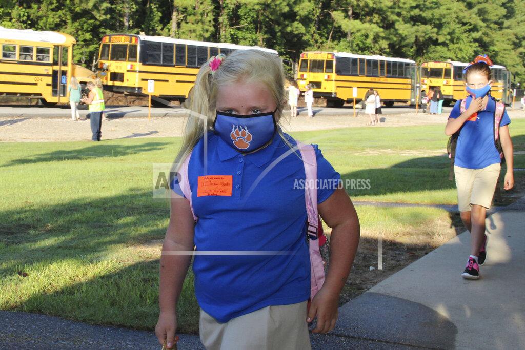 Janine Vincent Following direction, McCartney Moulds, 6, a second-grader, distances herself from a fellow student as she walks to class with full mask following her bus commute, to the Newton County Elementary School in Decatur, Miss., Monday, Aug. 3, 2020. Thousands of students across the nation are set to resume in-person school Monday for the first time since March. Parents are having to balance the children's need for socialization and instruction that school provides, with the reality that the U.S. death toll from the coronavirus has hit about 155,000 and cases are rising in numerous places. (Janine Vincent/Newton County Schools via AP)