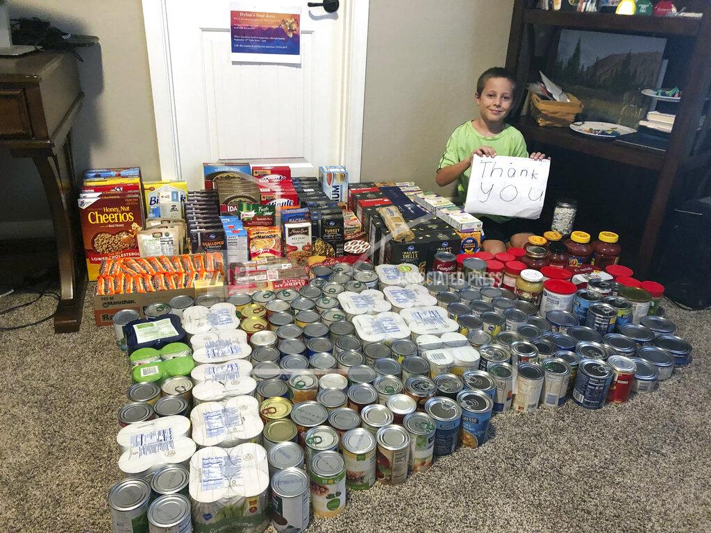 Erin Pfeifer Dylan Pfeifer sits with all the donations he received during his first food drive at his home in Chandler, Ariz., in October 2020. Pfeifer received 316 cans and boxes of food. Each drive is the culmination of hours of work that involves drawing posters, going door-to-door to hand out flyers and working with his mother to post information on Facebook. (Erin Pfeifer via AP)