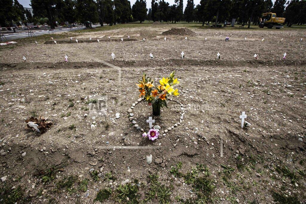 Luca Bruno FILE - In this May 8, 2020 file photo, flowers and stones placed in the shape of a heart are laid on a burial site as white crosses are scattered at the Campo 81, an area created to host COVID-19 victims, at the Maggiore cemetery in Milan, Italy. Italy is poised to reclaim the dishonor of reporting the most coronavirus deaths in Europe, as the second surge ravages the country’s disproportionately old population and exposes how public health shortfalls and delayed restrictions compounded a lack of preparedness going into the pandemic. (AP Photo/Luca Bruno, file)