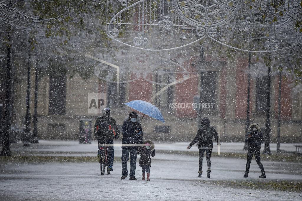 Alvaro Barrientos People wearing face mask protection to prevent the spread of coronavirus as snow falls in the city, in Pamplona, northern Spain, Saturday, Dec. 5, 2020. (AP Photo/Alvaro Barrientos)