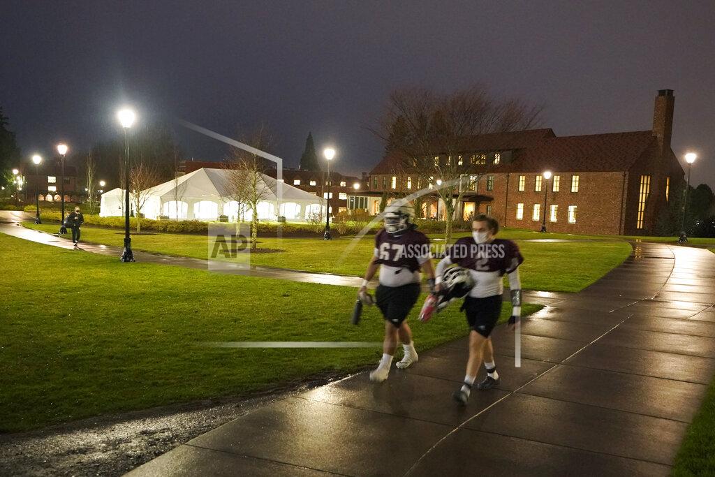 Ted S. Warren Two players walk near a large white tent used for COVID-19 testing as they head to a field for NCAA college football practice at the University of Puget Sound, Tuesday, Feb. 2, 2021, in Tacoma, Wash. School athletics officials are fully aware one infection could derail the season. (AP Photo/Ted S. Warren)