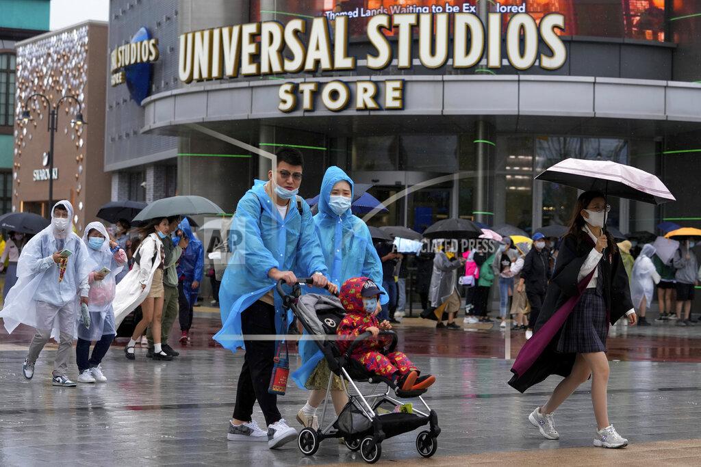 Andy Wong A family wearing raincoats and face masks to help protect from the coronavirus walk by masked visitors lining up to enter a Universal Studios store as they visit Universal Studios Beijing in Beijing, Monday, Sept. 20, 2021. Thousands of people brave the rain visit to the newest location of the global brand of theme parks which officially opens on Monday. (AP Photo/Andy Wong)
