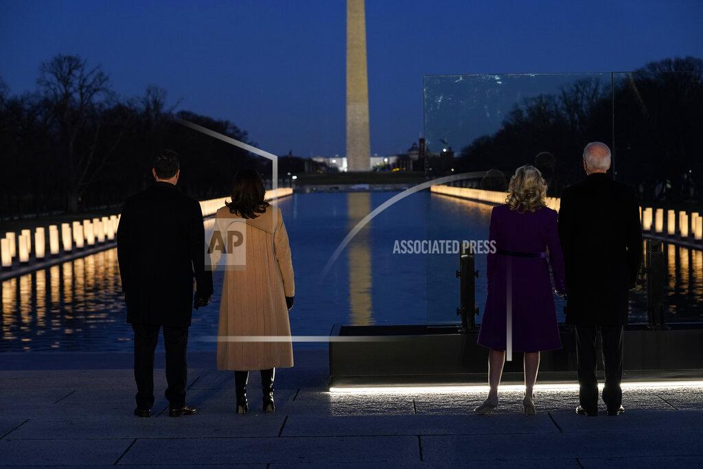 Evan Vucci With the Washington Monument in the background, President-elect Joe Biden stands with his wife Jill Biden and Vice President-elect Kamala Harris stands with her husband Doug Emhoff as they look at lights placed around the Lincoln Memorial Reflecting Pool during a COVID-19 memorial Tuesday, Jan. 19, 2021, in Washington. (AP Photo/Evan Vucci)