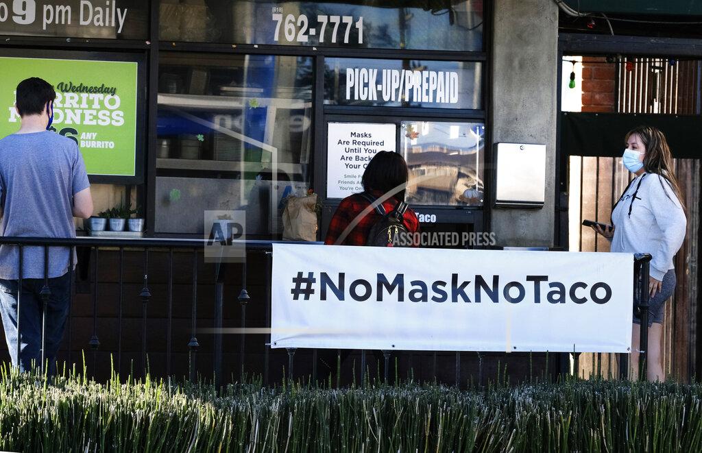 Richard Vogel Masked customers wait for their take out order at Hugo's Tacos in the Studio City section of Los Angeles on Sunday Dec. 6, 2020. Many Californians were preparing Sunday for a new stay-at-home order that bars restaurant dining, shutters salons and limits retail in an effort to curb spiraling coronavirus infections and hospitalizations. (AP Photo/Richard Vogel)