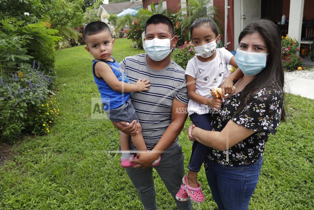 In this Sunday, June 7, 2020, photo, Elbin Sales, second from left, poses for a photograph with his wife, Yecenia Solorzano, right, and children Jordi Sales, left, and Athena Sales, amid the new coronavirus pandemic in Immokalee, Fla. Sales, who works as a landscaper, tested positive for COVID-19 and is quarantined at home with his family. Even as the pace of new cases has moderated in the state of Florida, this poor farmworking town in rural Florida is in the throes of an outbreak. (AP Photo/Lynne Sladky)