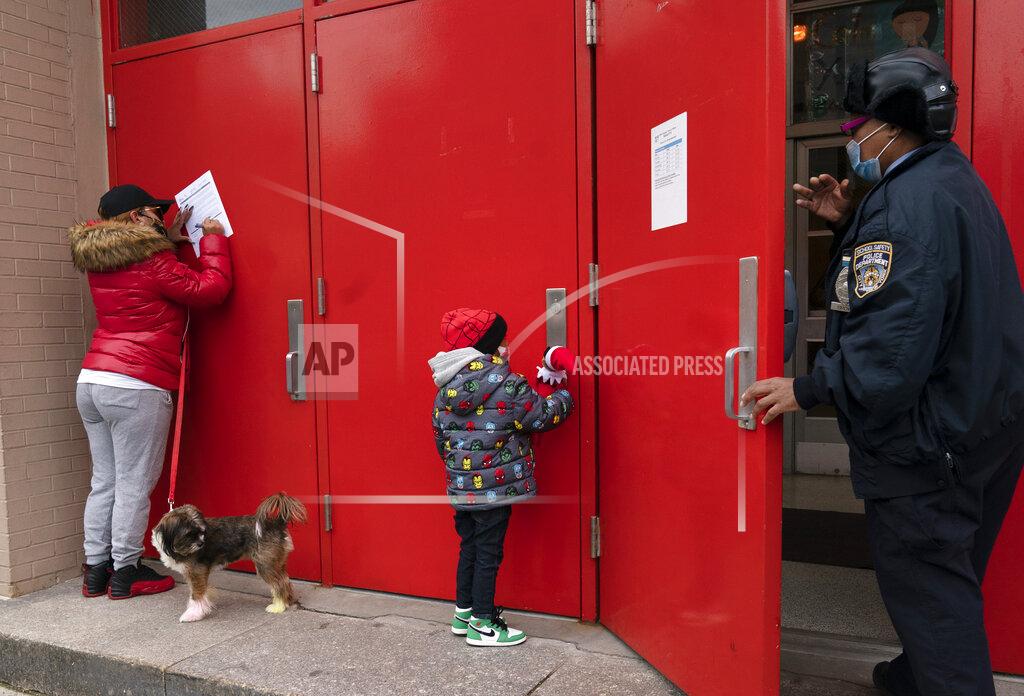 Mark Lennihan Sheila Melendez, left, completes a form granting permission for random COVID-19 testing for students as she arrives with her daughter Jayceon, center, at P.S. 134 Henrietta Szold Elementary School, Monday, Dec. 7, 2020, in New York. Public schools reopened for in-school learning Monday after being closed since mid-November. (AP Photo/Mark Lennihan)