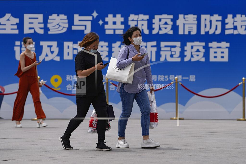 Andy Wong Women wearing face masks to help curb the spread of the coronavirus walk by a billboard showing the words "All people participate in building a line of defense against the epidemic, please get the vaccine in time" on display outside a shopping mall in Beijing, Monday, May 24, 2021. (AP Photo/Andy Wong)