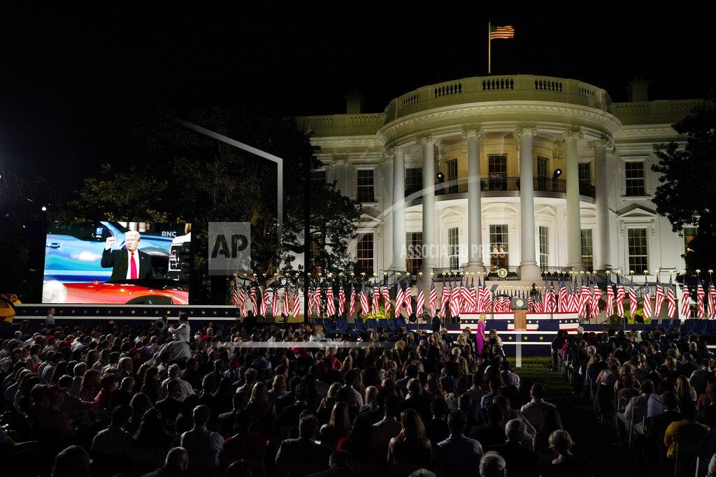 People watch video screens before President Donald Trump speaks from the South Lawn of the White House on the fourth day of the Republican National Convention, Thursday, Aug. 27, 2020, in Washington. (AP Photo/Evan Vucci)
