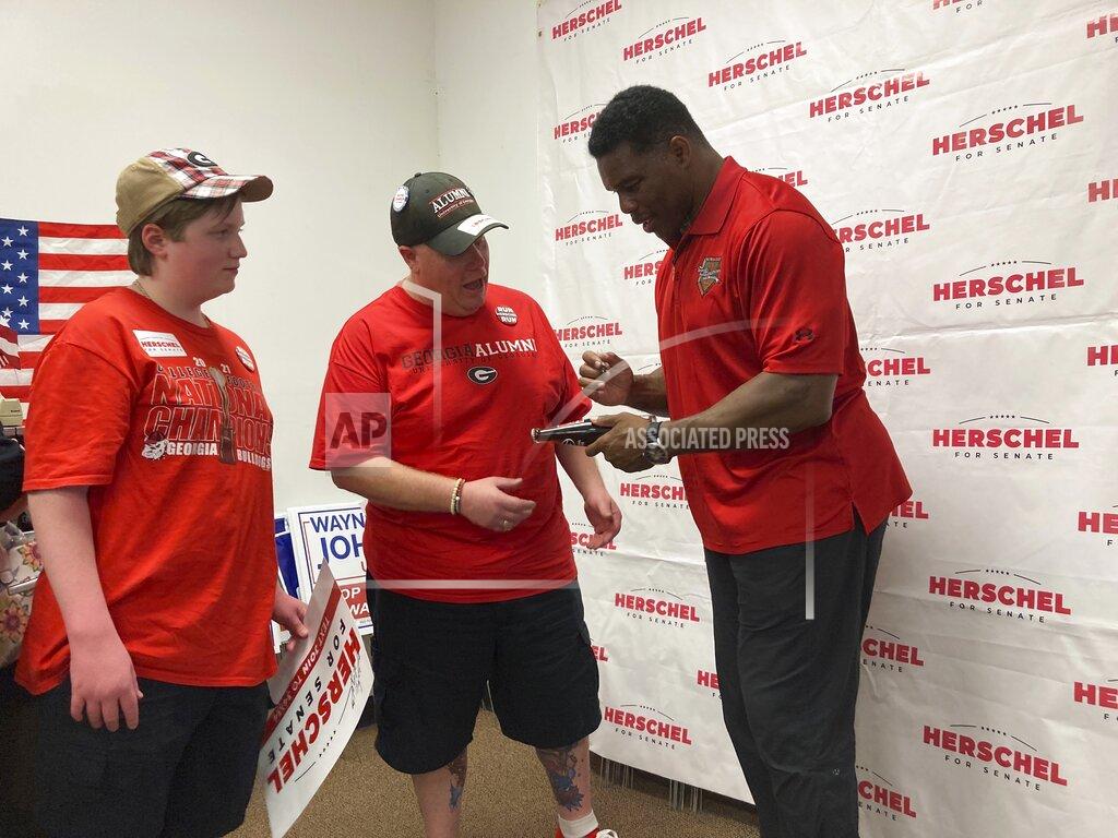 Jeff Amy Georgia Republican Senate candidate Herschel Walker, right, signs a soda bottle commemorating the 1980 football championship he won with the University of Georgia for Peter Bagarella of Ellerslie, Ga., after a speech at Muscogee County GOP headquarters in Columbus, Ga., Saturday, May 21, 2022. (AP Photo/Jeff Amy)
