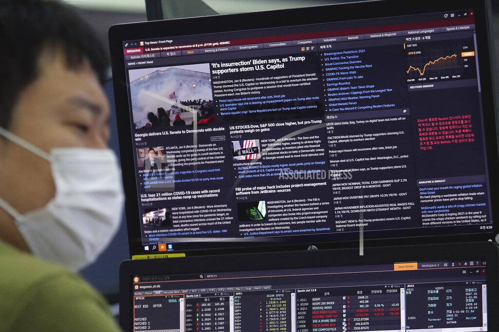 Ahn Young-Joon A currency trader works in front of a screen which shows a report on a mob by U.S. President Donald Trump supporters, at the foreign exchange dealing room of the KEB Hana Bank headquarters in Seoul, South Korea, Thursday, Jan. 7, 2021. (AP Photo/Ahn Young-joon)