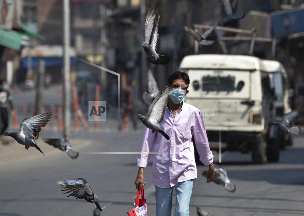 Mukhtar Khan Pigeons fly as a man wearing a mask walks past in Srinagar, Indian controlled Kashmir, Monday, July 13, 2020. Authorities reimposed lockdown on Monday in parts of Indian-controlled Kashmir, including the region's main city, following surge in coronavirus cases. (AP Photo/Mukhtar Khan)