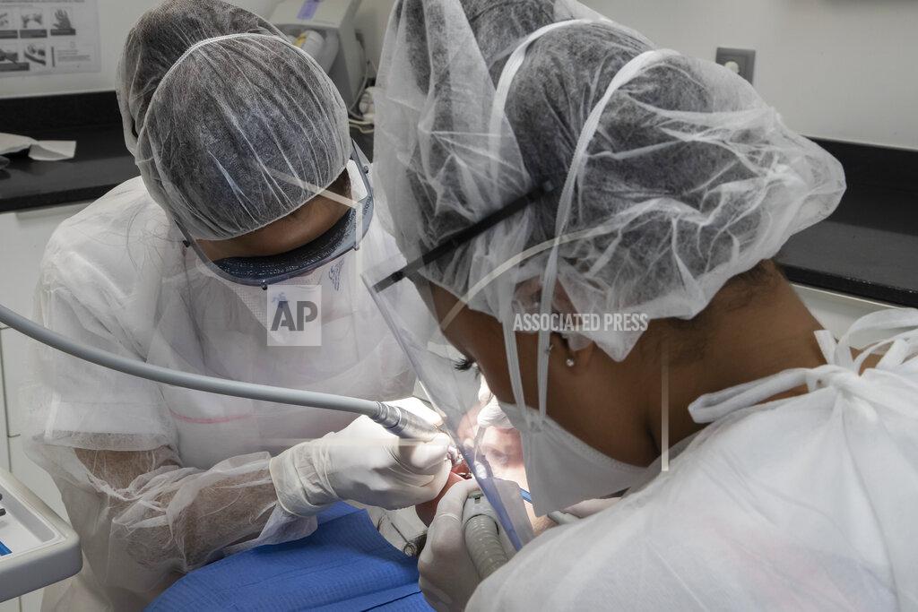 Michel Euler In this Wednesday, May 13, 2020 photo, dentist Sabrine Jendoubi, left, and her dental assistant Margot Daussat inspect the teeth of patient Veronique Guillot, during a dental appointment at a dental office in Paris. Those with toothache that suffered through France's two-month lockdown, finally have hope to end the pain. Dental practices are cautiously re-opening and non-emergency dentist appointments are now permitted around the country, as the French government eased confinement restrictions from Monday. (AP Photo/Michel Euler)