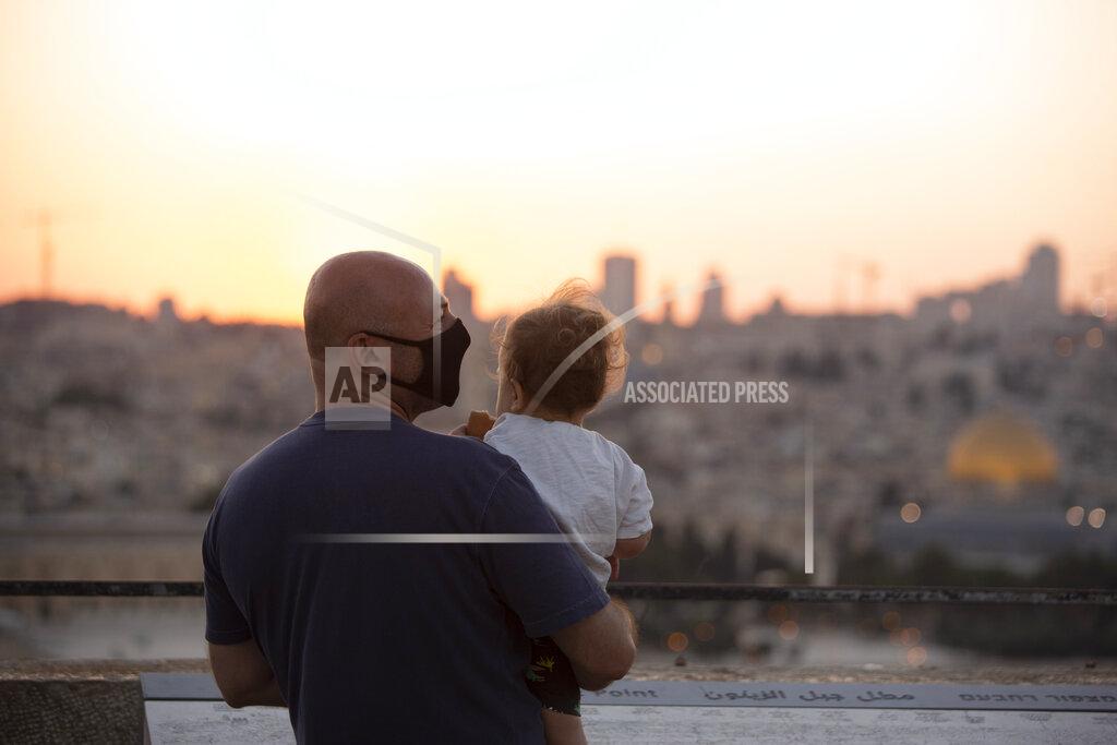 Maya Alleruzzo A man wearing a mask to curb the spread of the coronavirus, holds a child on an overlook at the Mount of Olives as they watch the sun set behind the Dome of the Rock Mosque in Jerusalem, Wednesday, Sept. 2, 2020. (AP Photo/Maya Alleruzzo)