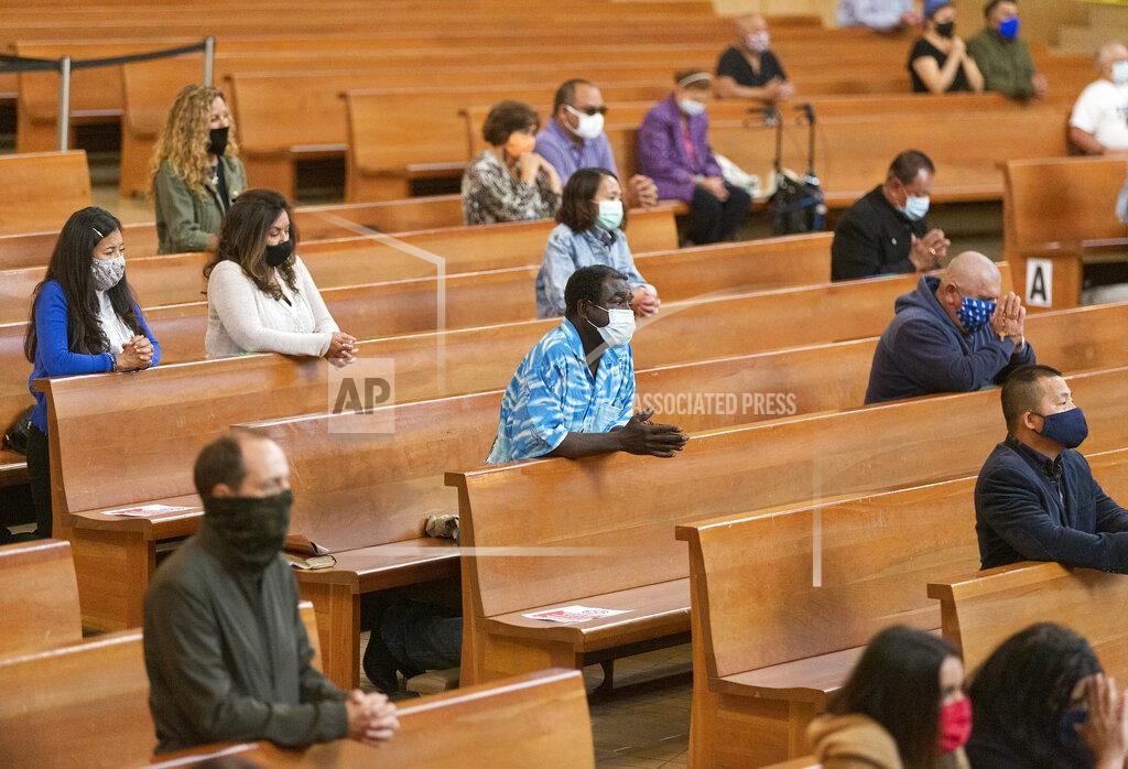 Damian Dovarganes FILE - Congregants kneel and observe social distancing while listening to Los Angeles Archbishop Jose H. Gomez celebrate Mass at Cathedral of Our Lady of the Angels in downtown Los Angeles, Sunday, June 7, 2020. A religious freedom law firm with ties to President Donald Trump says it will sue California over its recent ban on singing or chanting in the church to slow the spread of the coronavirus. (AP Photo/Damian Dovarganes, File)