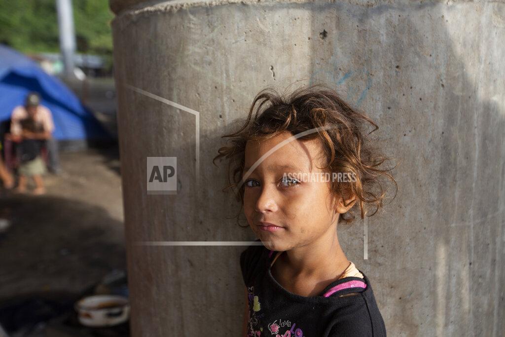 Moises Castillo Katerine waits for breakfast cooked by her family under a bridge on the outskirts of San Pedro Sula, Honduras, Monday, Jan. 11, 2021. The 9-year-old has lived under this bridge with her family since they lost their home to last year's hurricanes Eta and Iota in November. (AP Photo/Moises Castillo)