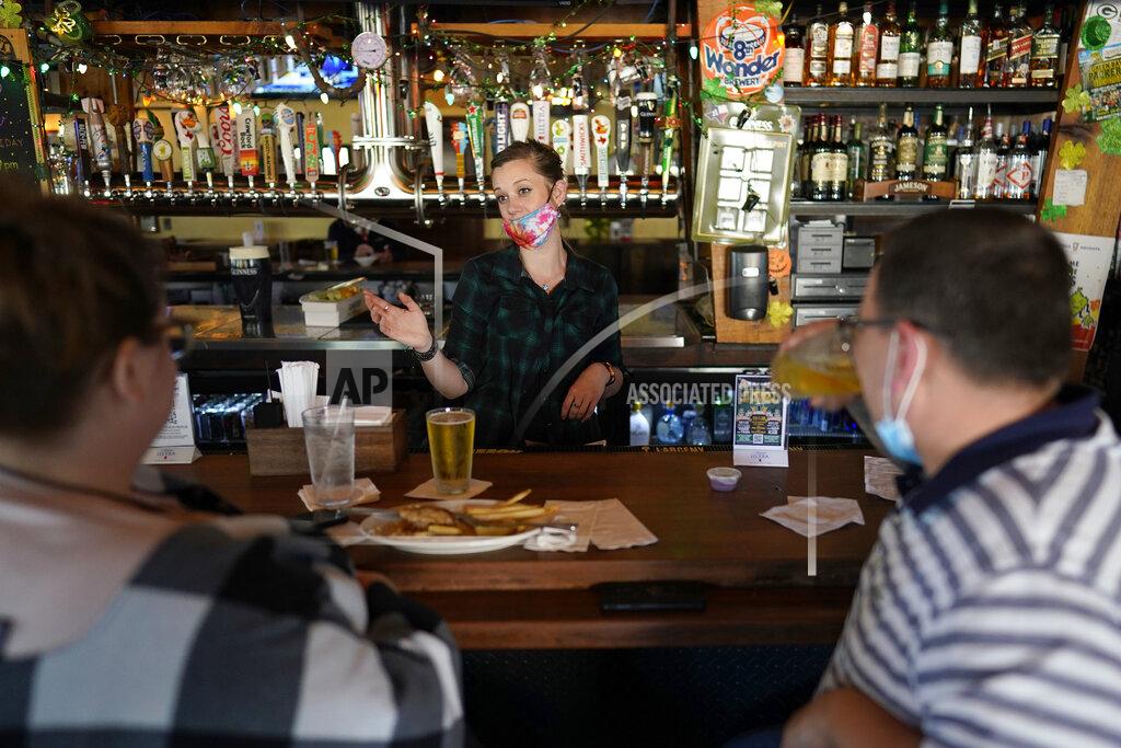 David J. Phillip Bartender Alyssa Dooley, center, talks with customers at Mo's Irish Pub, Tuesday, March 2, 2021, in Houston. Texas Gov. Greg Abbott announced that he is lifting business capacity limits and the state's mask mandate starting next week. (AP Photo/David J. Phillip)