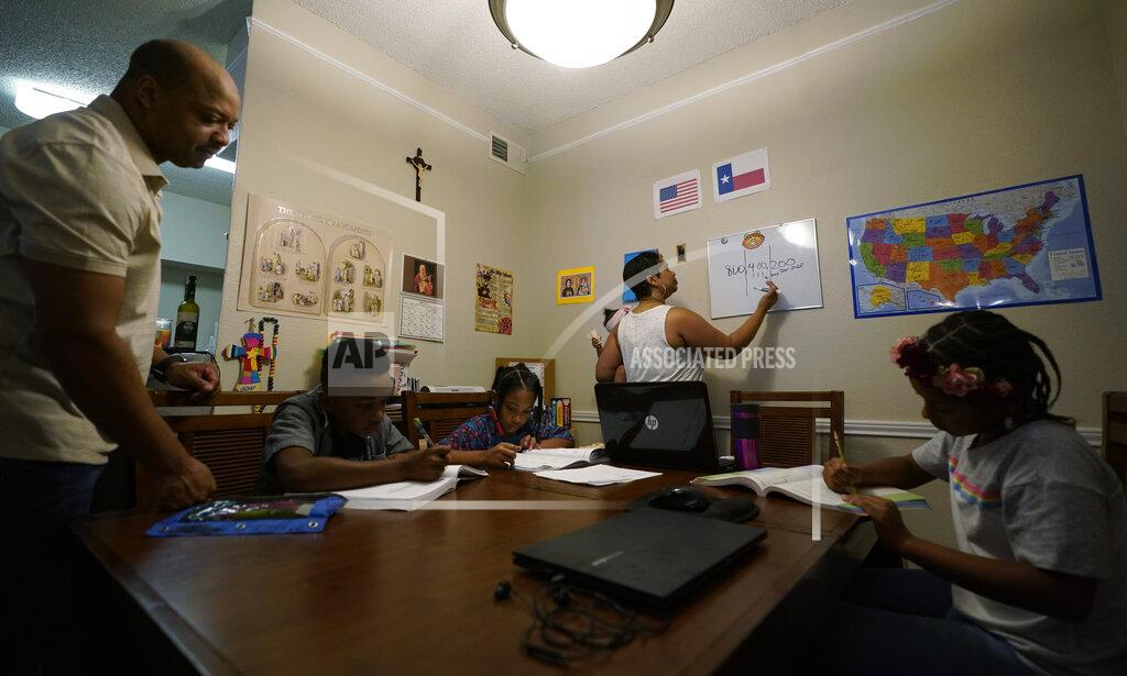 Eric Gay Arlena Brown, center, holds her youngest child, Lucy, 9 months, as she and husband, Robert, left, lead their other children, from left, Jacoby, 11; Felicity, 9, and Riley, 10, through math practice at their home in Austin, Texas, Tuesday, July 13, 2021. “I didn’t want my kids to become a statistic and not meet their full potential,” said Robert, a former teacher who now does consulting. “And we wanted them to have very solid understanding of their faith.” (AP Photo/Eric Gay)