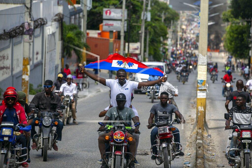 Dieu Nalio Chery A protester holds up a Haitian national while riding on a motorcycle during a protest to demand the resignation of President Jovenel Moise in Port-au-Prince, Haiti, Saturday, Oct. 17, 2020. The country is currently experiencing a political impasse without a parliament and is now run entirely by decree under Moise. ( AP Photo/Dieu Nalio Chery)