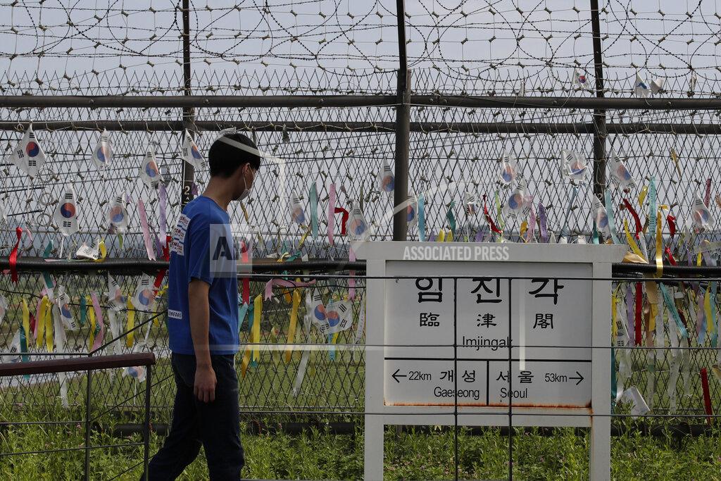 A visitor walks in front of a directional sign showing the distance to North Korea's Kaesong city and South Korea's capital Seoul near the wire fences decorated with ribbons written with messages wishing for the reunification of the two Koreas at the Imjingak Pavilion in Paju, South Korea, Sunday, June 14, 2020. South Korea on Sunday convened an emergency security meeting and urged North Korea to uphold reconciliation agreements, hours after the North threatened to demolish a liaison office and take military action against its rival. (AP Photo/Lee Jin-man)