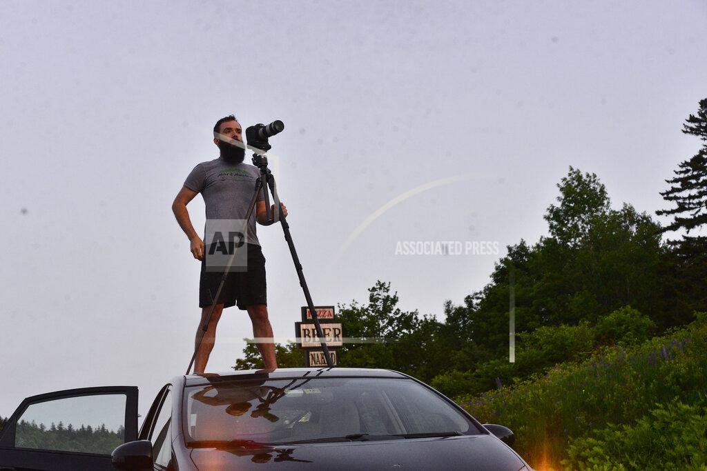 Kristopher Radder Josh Fields, from Putney, Vt., stands on top of his vehicle to get a clear photograph of the the partial solar eclipse at Hogback Mountain, in Marlboro, Vt., on Thursday, June 10, 2021. (Kristopher Radder/The Brattleboro Reformer via AP)