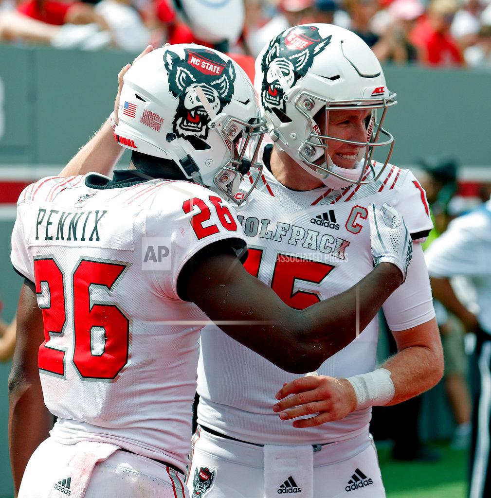 Chris Seward FILE - In this Sept. 8, 2018, file photo, North Carolina State's Trent Pinnix (26) celebrates his touchdown with Ryan Finley (15) after he scored during the second half of an NCAA college football game, in Raleigh, N.C. The showdown between Will Grier and Ryan Finley could be wrecked by Hurricane Florence. No. 14 West Virginia’s visit to North Carolina State looked like a high-scoring shootout _ with the NFL-caliber quarterbacks flinging the ball around to a bunch of talented receivers _ but that was before a hurricane took aim at the East Coast(AP Photo/Chris Seward, File)