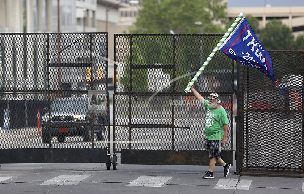 Mike Simons Mike Pellerin waves a Donald Trump campaign flag near a barricade in downtown Tulsa, Okla., ahead of President Donald Trump's Saturday's campaign rally Friday, June 19, 2020. (Mike Simons/Tulsa World via AP)