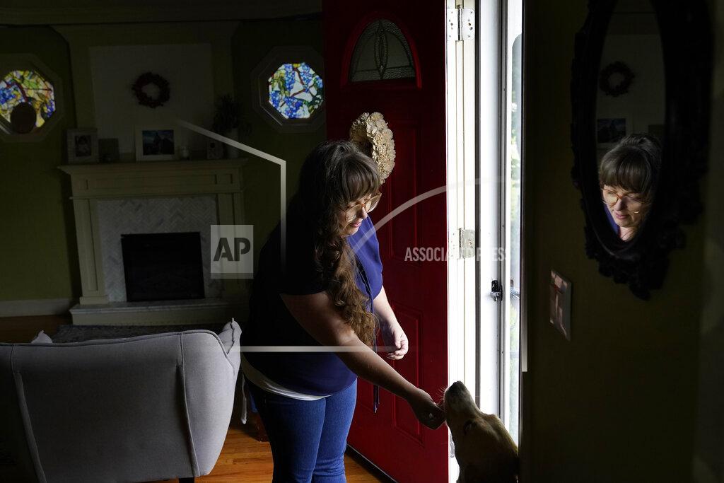 Steven Senne Allison Cullen, of Brockton, Mass., greets the family dog Lula, right, Thursday, July, 22, 2021, after speaking on the phone with her husband Flavio Andrade Prado, a Brazilian national, from their home in Brockton. Prado is being held by Immigration and Customs Enforcement, or ICE, at the Plymouth County House of Corrections. The number of detainees nationwide has more than doubled since the end of February, to nearly 27,000, according to recent data from U.S. Immigration and Customs Enforcement. (AP Photo/Steven Senne)