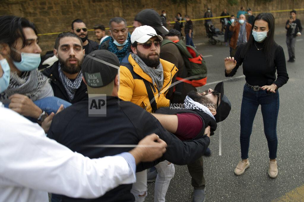 Hassan Ammar Protestors hold an injured man during a scuffle between riot police and anti-government protesters outside a military court, in Beirut, Lebanon, Monday, Feb. 8, 2021. Riot police briefly clashed Monday in Beirut with hundreds of protesters demanding the release of anti-government activists detained following riots in northern Lebanon late last month. (AP Photo/Hassan Ammar)