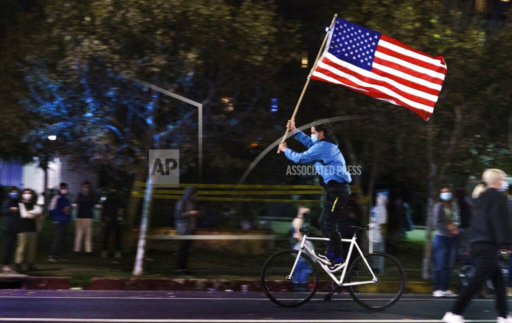 Damian Dovarganes A supporter of President-elect Joe Biden and Vice President-elect Kamala Harris rides standing on his bicycle as he parades with the flag on Sunset Blvd., in Los Angeles late Saturday, Nov. 7, 2020. Democrat Joe Biden defeated President Donald Trump to become the 46th president of the United States on Saturday, positioning himself to lead a nation gripped by the historic pandemic and a confluence of economic and social turmoil. (AP Photo/Damian Dovarganes)