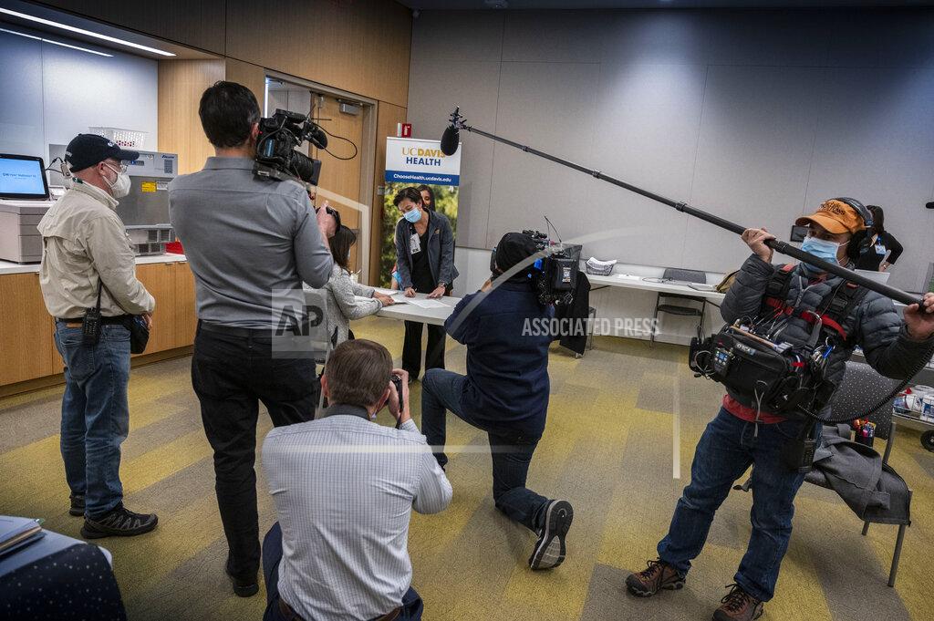 Hector Amezcua Eva Teniola , UC Davis Medical Center Emergency Department Registered Nurse, is surrounded by members of the press before she is the first person in the state be inoculated with the PPfizer-BioNTech COVID-19 vaccine at the UC Davis Medical Center, Tuesday, Dec. 15, 2020 in Sacramento, Calif. (AP Photo/Hector Amezcua, Pool)