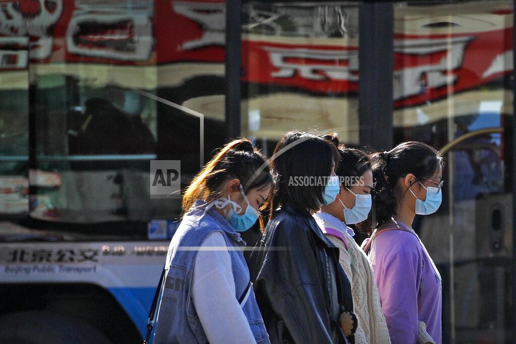 Andy Wong Women wearing face masks to help curb the spread of the coronavirus walk along a moving bus on a street in Beijing, Wednesday, Oct. 28, 2020. (AP Photo/Andy Wong)