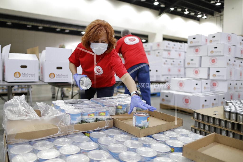 Laura Anderson grabs a can of food for a box, Tuesday, May 12, 2020, in Indianapolis. The Salvation Army, with the help of the Midwest Food Bank and the Indiana National Guard, packed 5,000 boxes at Lucas Oil Stadium to help Hoosier families in need. (AP Photo/Darron Cummings)