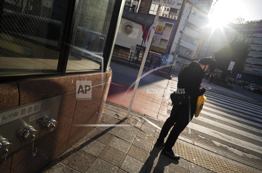 Hiro Komae A man wearing a face mask looks at his cellphone while waiting to walk across an intersection during the coronavirus state of emergency in Tokyo on Thursday, Jan. 14, 2021. (AP Photo/Hiro Komae)