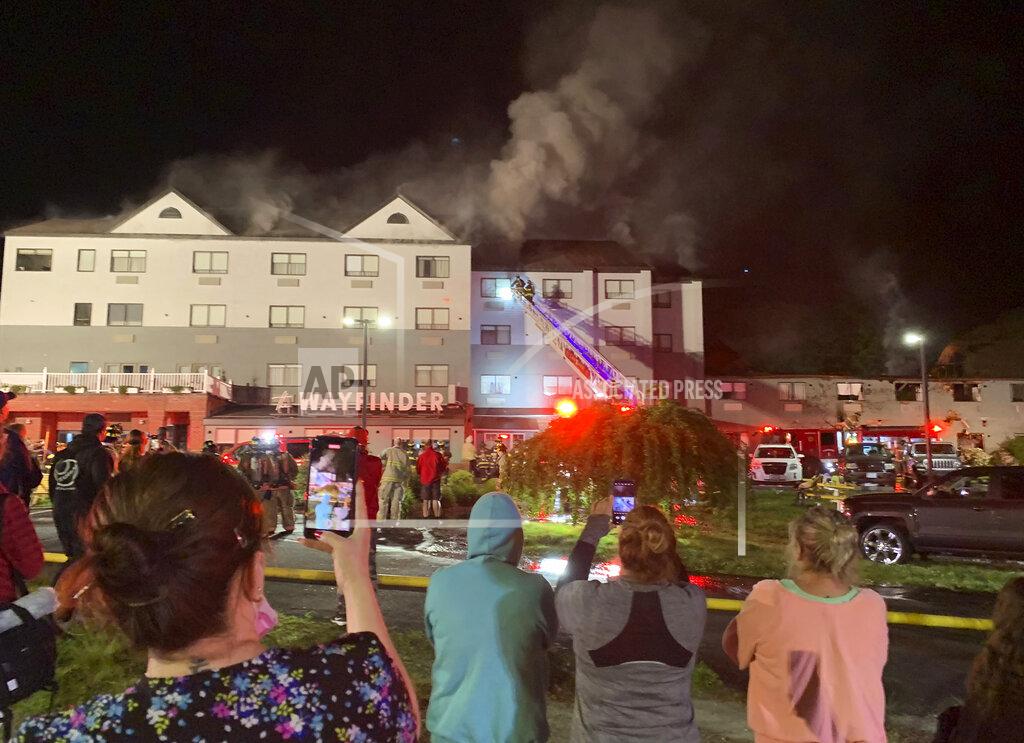 Scott Barrett People look on as firefighters battle a fire at a recently renovated hotel in Newport, R.I., Monday, May 23, 2022. Three firefighters were injured battling the fire at the Wayfinder Hotel. (Scott Barrett/The Newport Daily News via AP)