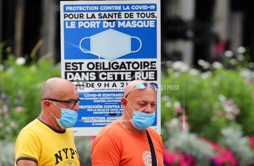 Bob Edme People wearing face masks to protect against coronavirus walk past a sign stating face coverings are required in the street, in Bayonne, southwestern France, Wednesday, July 28, 2021. Local authorities in France are re-imposing mask mandates and other virus restrictions because of fast-growing infections with the delta variant, which is causing COVID-19 hospitalizations in France to rise again. (AP Photo/Bob Edme)