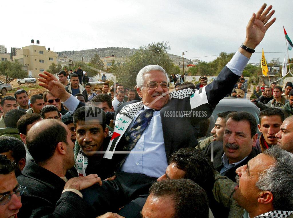Enric Marti FILE - In this Dec. 30, 2004 file photo, then Interim Palestinian leader Mahmoud Abbas, and front-runner in the upcoming presidential elections, is carried by the Al Aqsa Martyrs' Brigades leader in West Bank, Zakaria Zubeidi, center left, during a campaign visit to the Jenin refugee camp. For nearly two decades, Zubeidi has been an object of fascination for Israelis and Palestinians alike, who have seen his progression from a child actor to a swaggering militant, to the scarred face of a West Bank theater promoting “cultural resistance” to Israeli occupation. In his latest act, he has emerged as one of Israel's most wanted fugitives after tunneling out of a high-security prison on Monday, Sept. 6, 2021 with five other Palestinian militants. (AP Photo/Enric Marti, File)
